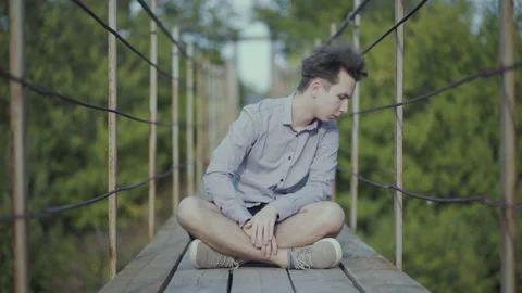 Guy sits on suspended bridge in the forest Stock Footage 139016820