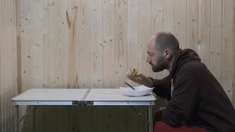 The guy sits at the table and eats from a plate mysteriously looking forward Stock Footage 119831802