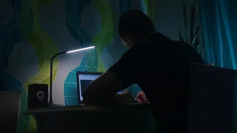 Guy sits table and writes, in front laptop. Evening, night, apartment table lamp Stock Footage 121360484