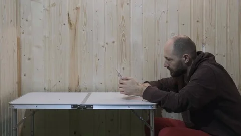 Guy sits at the table in room and plays in phone Stock Footage 119550395