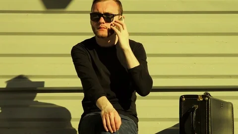 Guy Sits on Train Station Bench With Bag and Talks on Smartphone Stock Footage 78557695
