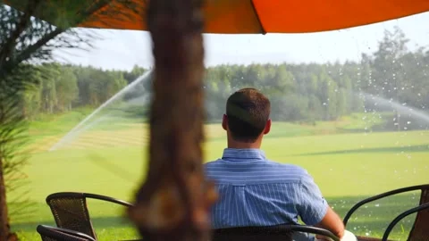 The guy sits under a canopy on the golf course while watering the lawn Stock Footage 197860000