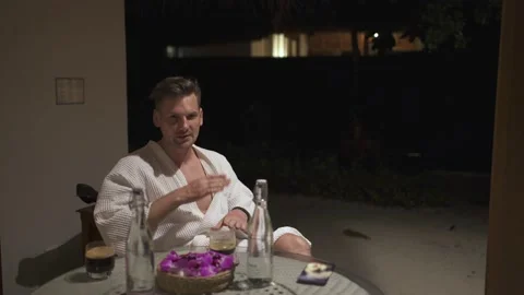 The guy sits on the veranda at night in a robe and coffee Stock Footage 146706966
