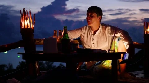 The guy sitting at the bar after sunset listening to music. Evening time 動画素材 75054057