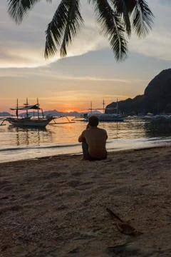 A guy sitting on the beach during sunset and taking pictures of the evening l Stock Photos