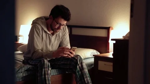 The guy sitting on the bed in the bedroom and looks at the phone Stock Footage 73515452