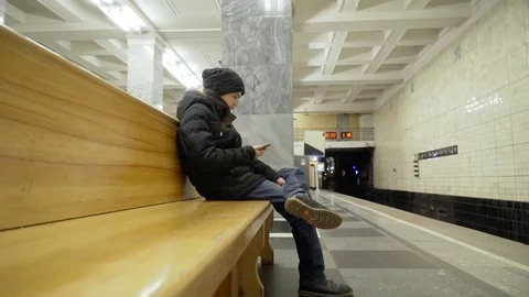 The guy is sitting on a bench in the metro putting his foot on his leg. A Stock Footage 82460572