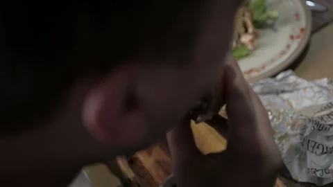 The guy is sitting in a cafe and eating a burger. Burger in hand and bite Stock Footage 109264243