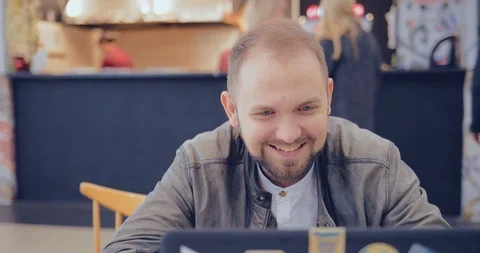 Guy is sitting in a cafe with a laptop and talking to someone Stock Footage 95970386