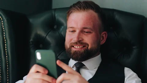 The guy is sitting in a chair and smiling looking at the smartphone screen Stock Footage 221200100