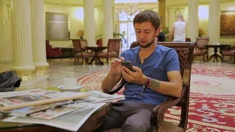 Guy sitting in chair in lobby of hotel, planning his sightseeing route for day Stock Footage
