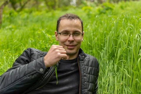 Guy sitting on grass with a blade of grass in his teeth Stock Photos