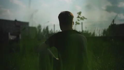 The guy is sitting in the grass at the edge of the path outside the city Видео 230191169