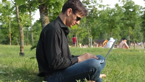 Guy is sitting on the grass with a laptop and typing Stock Footage 135238217