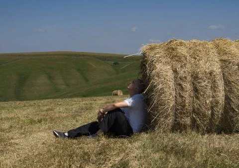 The guy is sitting on the grass near a haystack in the summer Stock Photos
