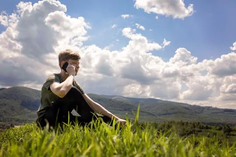 The guy is sitting on the mountain and talking on a mobile phone. Stock Photos