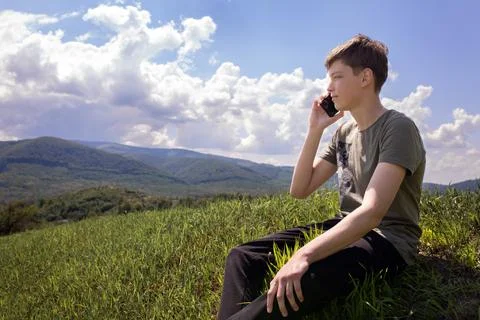 The guy is sitting on the mountain and talking on a mobile phone. Stock Photos