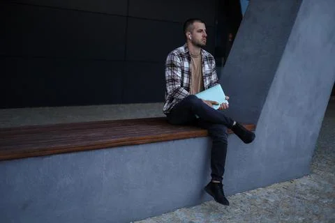The guy is sitting near office buildings and working on a laptop Stock Photos