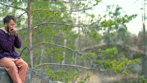 Guy sitting on the rock and playing on the harmonica. Video stock 106190337