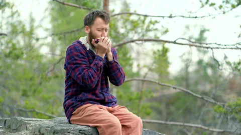 Guy sitting on the rock, playing on the harmonica. Video stock 106092706