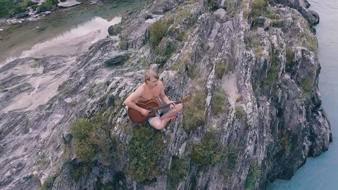 The guy sitting on the rocks and playing guitar by the river in the highlands Stock Footage 93734581