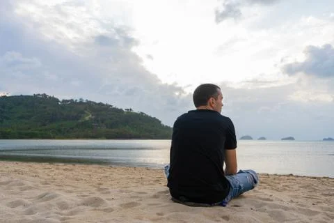 A guy is sitting on a sandy beach looking at the water. Enjoys the beautiful  Stock Photos