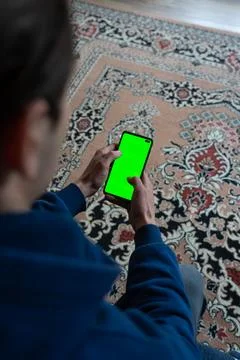 Guy is sitting with a smartphone in his hands with the green screen turn on Stock Photos
