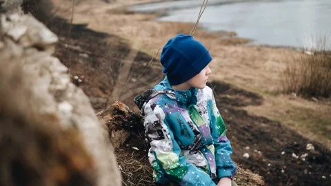 The guy is sitting on a steep slope by the river and looks at nature 스톡 동영상 128016586