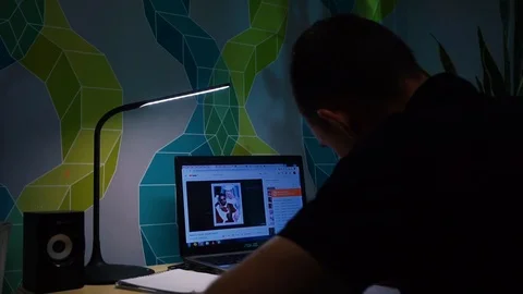 Guy sitting at table, in front of a laptop, writes a text on a sheet with a pen Stock Footage 121360522