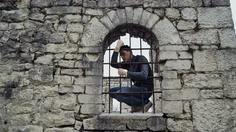Guy is sitting on the window behind the bars in the fortress and trying to get Vídeo Stock 113979493