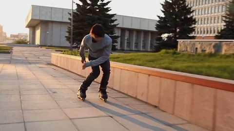 The guy slides on the roller skates on the parapet in the rays of the setting 库存影片 87253700