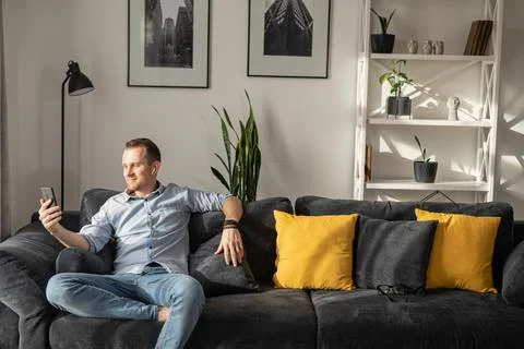 A guy with a smartphone sits on the couch Foto stock