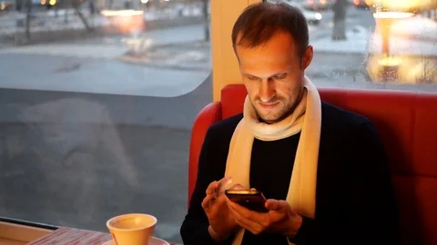 The guy with the smartphone sits at the table and drinks coffee 動画素材 102545260