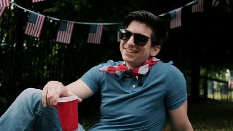 Guy smiling and holding plastic cup with american flags in the background Video stock 133614936