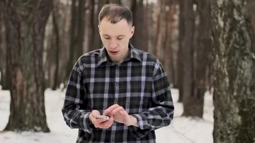 Guy in the snow-covered cold forest with a mobile phone Stock Footage 85516778