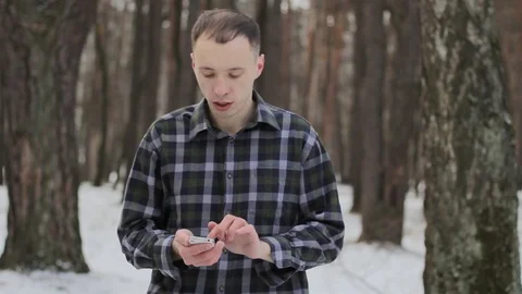 A guy in a snowy forest communicates on a mobile device 스톡 동영상 85517000