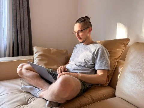 Guy software developer working behind a laptop on a sofa in a cozy apartment Foto stock