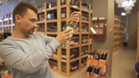 Guy is spinning a bottle of wine, evaluating its quality at a wine store. Video stock 99385091