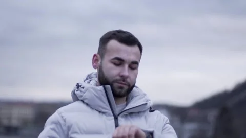 A guy is standing and looking at his watch. A guy in a white jacket Stock Footage 130743285