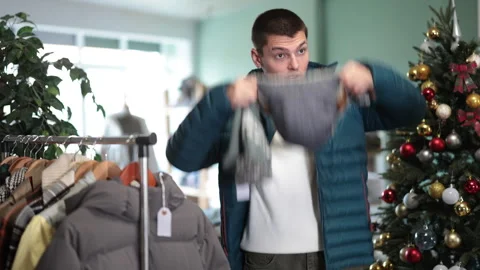 Guy is standing in a clothing store against the background of a Christmas tree Stock Footage 329398566