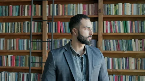 Guy Is Standing In The Library. Attractive Brunette With Beard From The Middle Stock Footage 140220928