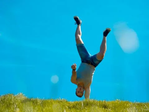 The guy is standing on one hand. Background blue sky. Below the green grass Foto stock