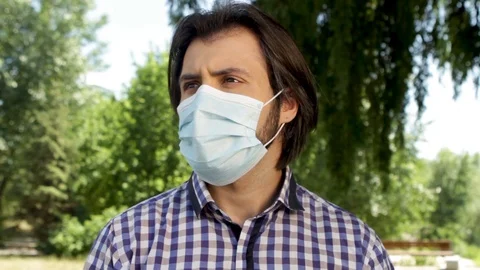 Guy is standing in park and wearing mask on face he is sick and looking to left Stock Footage 99740003