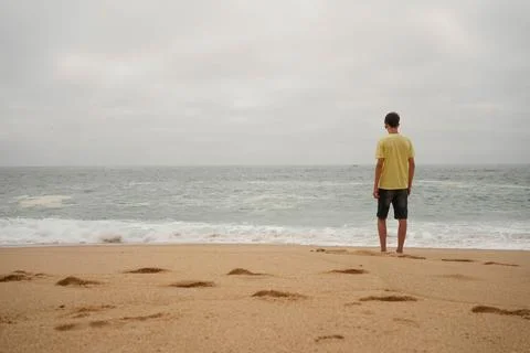Guy standing at a sandy beach looking over the ocean lonely Foto stock