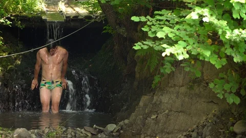 The guy is standing under a small waterfall. EMC on head flows down water Stock Footage 92803217