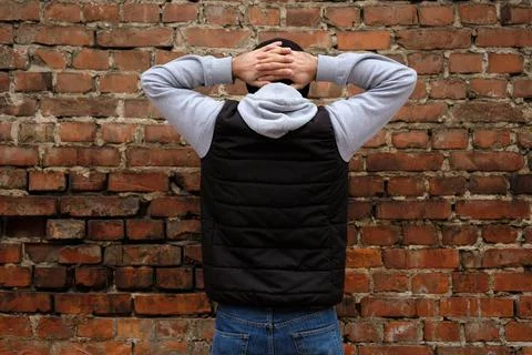 The guy stands facing a brick wall with his hands clasped behind his head Foto stock
