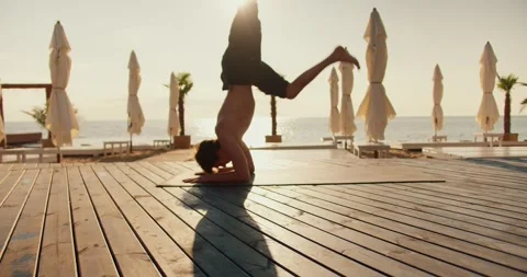 The guy stands on his head on a special mat on a sunny beach. Yoga classes Stock Footage 249435618
