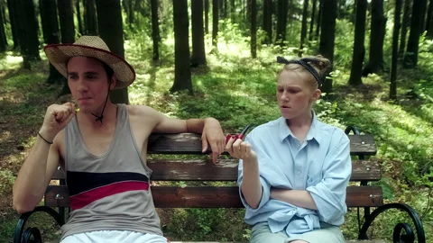 A guy in a straw hat and a girl in a blue shirt chat sitting on a bench Stock Footage 197481502