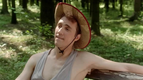 A guy in a straw hat sits on a bench in the woods Stock Footage 197481318