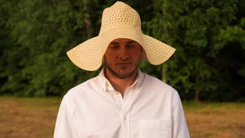 Guy in straw yellow hat is standing in a field, looking seriously at the camera Stock Footage 161690379
